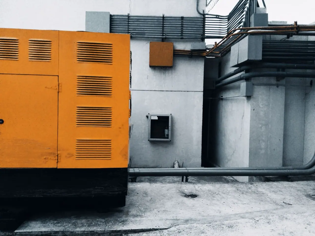 Orange canopy diesel generator set standing outdoors beside an industrial building